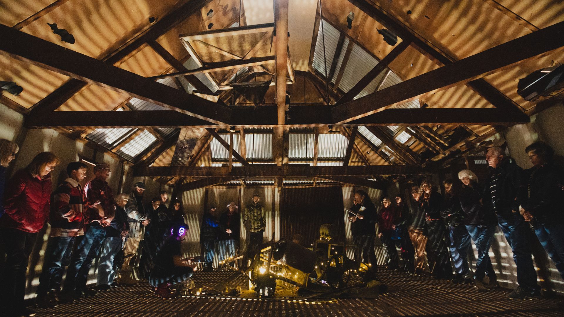 Audience gathered around a glowing art installation in a weathered Tasmanian shearing shed, 2019.