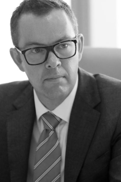 Isaac Poole in glasses and a suit and tie, measured expression, looking like someone who reads the fine print and finds things in it.