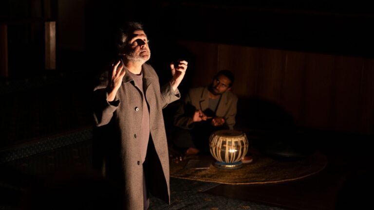 Actor on a stage with a musician sitting on the floor beside him with percussion instrument