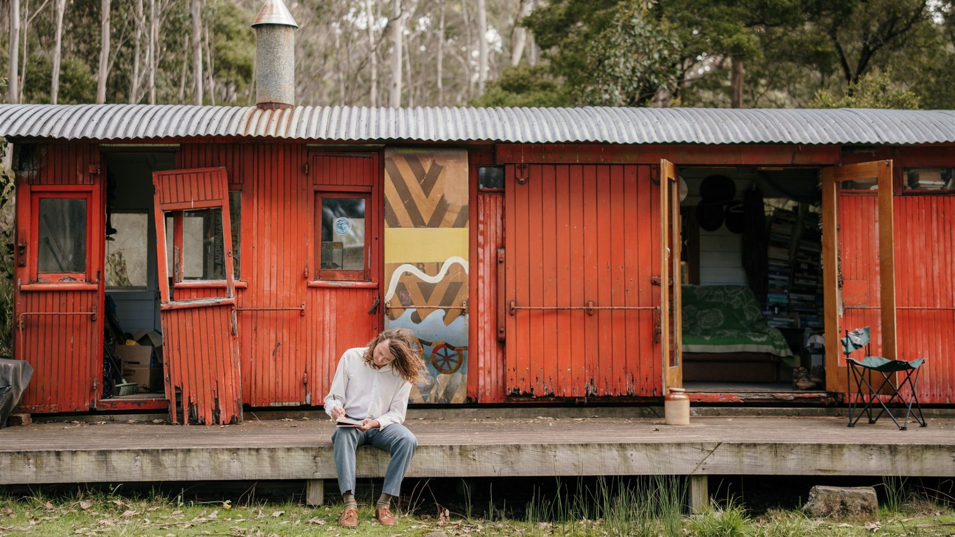 Bert Spinks sits on a deck in front of a rail carriage writing.